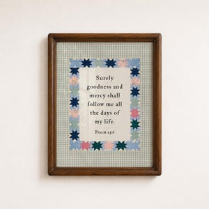 May include: A framed wall art print featuring the text "Surely goodness and mercy shall follow me all the days of my life. Psalm 23:6" centered on a cream background, surrounded by a border of blue, pink, and green star-shaped quilt patterns.