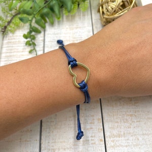 May include: A navy blue cord bracelet with a gold heart charm. The bracelet is adjustable and can be worn on any wrist.