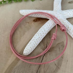 May include: A pink cord bracelet with a simple knot design. The bracelet is made of a soft, thin cord and is adjustable to fit most wrists.