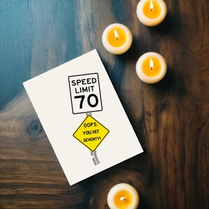 Celebrate their 70th birthday with a funny 'Oops You Hit 70' Birthday Card, shown next to glowing yellow candles. This charming combination adds a memorable touch to their special birthday.