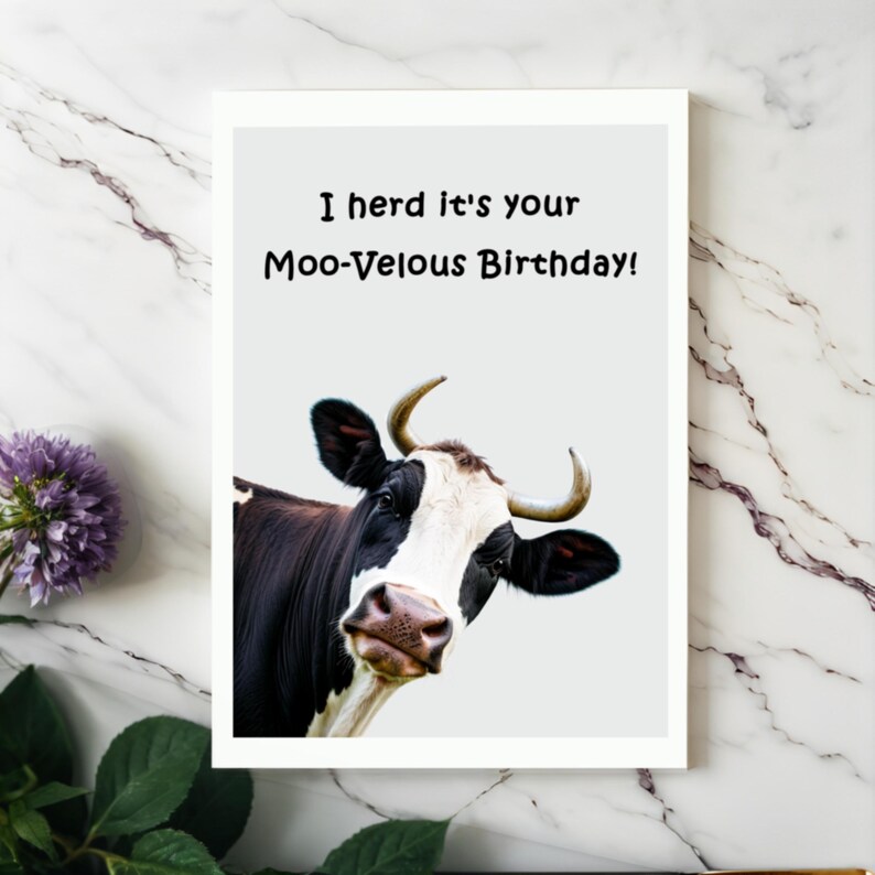 Showcased on a white granite countertop next to vibrant purple flowers, the Cow-themed Birthday Card adds a touch of charm and fun to any celebration.