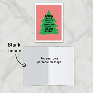 This Christmas card has a salmon-colored background that really pops against the large green Christmas tree silhouette in the center. The tree has a rough, hand-painted appearance with jagged edges, giving it a charming and homemade feel. In bold, black, handwritten-style font, the text "SANTA WORKS ONE DAY A YEAR, SPENDS THE REST OF IT JUDGING PEOPLE" . The card has been left blank to write your personalized message.