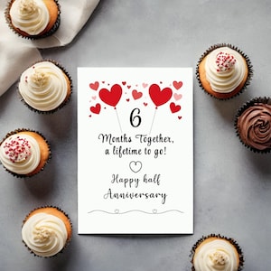 Celebrate  your 6-month anniversary with a card featuring red and pink hearts at the top and the heartfelt message, '6 months together, a lifetime to go!' This card is displayed next to several cupcakes on a table.