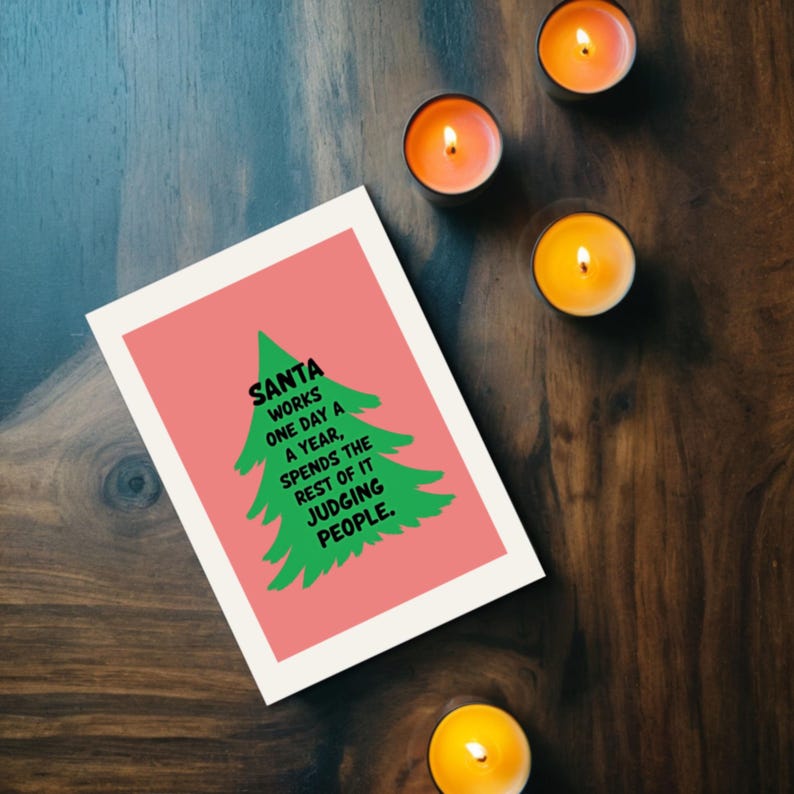 Whish someone a holiday with a cheerful Christmas card featuring a playful take on the holiday season! The card has a  background that really pops against the large green Christmas tree silhouette in the center. The tree has a rough, hand-painted appearance with jagged edges, giving it a charming and homemade feel. In bold, black, handwritten-style font, the text "SANTA WORKS ONE DAY A YEAR, SPENDS THE REST OF IT JUDGING PEOPLE". The card is next to candles.
