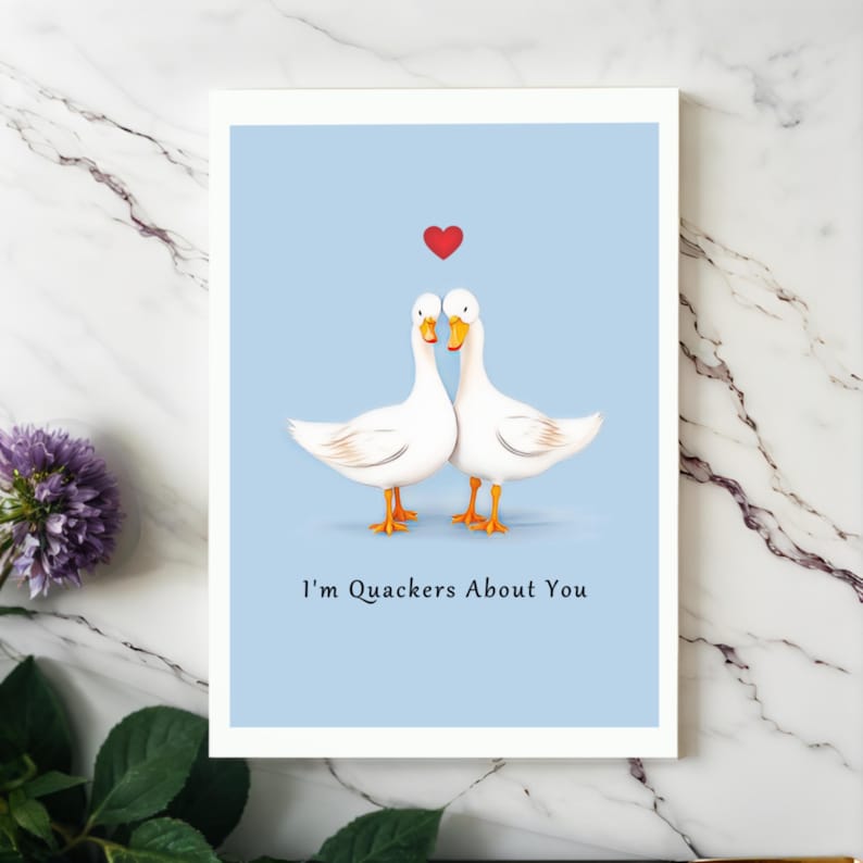 Showcased on a white granite countertop next to vibrant purple flowers, the Ducks in Love Anniversary Card adds a touch of charm and elegance to any special occasion.