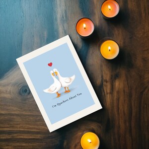 Set on a brown oak table with yellow and orange glowing candles, the Ducks in Love Anniversary Card brings a cozy and enchanting touch to the celebration