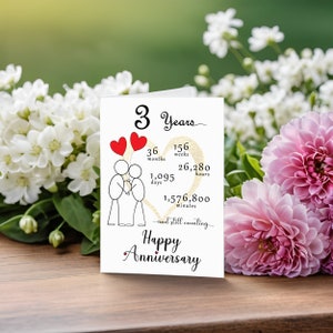 Celebrate your 3 year anniversary with an enchanting card featuring a gold heart, two intertwined heart balloons held by stick figures, and a backdrop of softly faded flowers for timeless elegance.