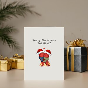 This card features two cute hot peppers hugging with a flame underneath and Santa hats for a holiday touch. The message Merry Christmas Hot Stuff adds a cute vibe, perfect for your partner this Christmas, showcased next to presents