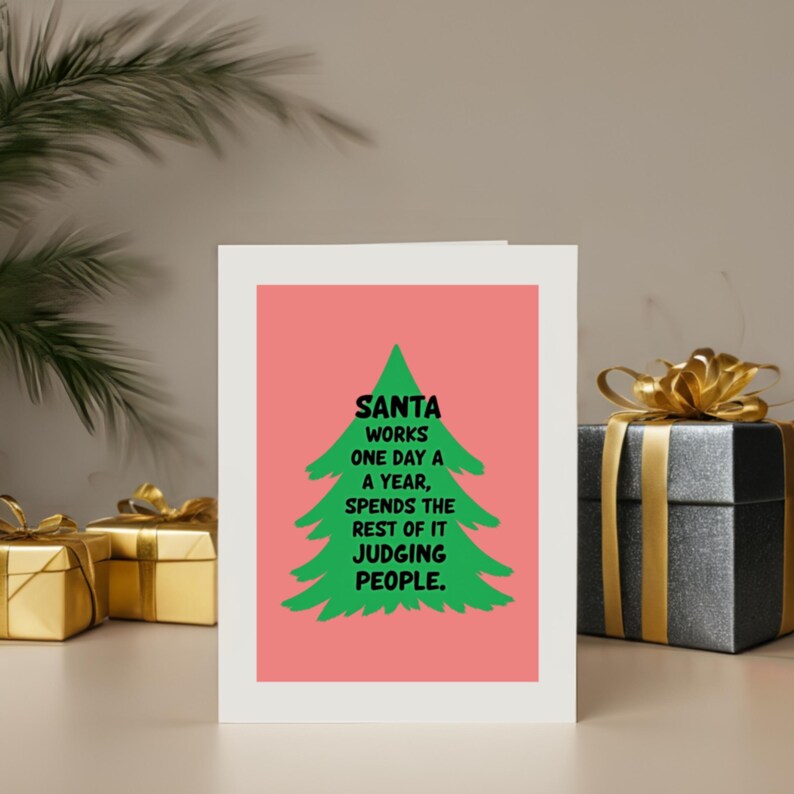 Whish someone a holiday with a cheerful Christmas card featuring a playful take on the holiday season! The card has a  background that really pops against the large green Christmas tree silhouette in the center. The tree has a rough, hand-painted appearance with jagged edges, giving it a charming and homemade feel. In bold, black, handwritten-style font, the text "SANTA WORKS ONE DAY A YEAR, SPENDS THE REST OF IT JUDGING PEOPLE". The card is next to presents.
