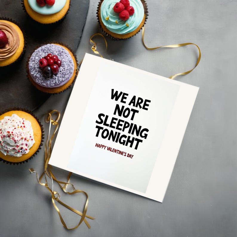 Valentine greeting card displayed next to cupcakes. The card features bold text stating We are not sleeping tonight on a clean white background.