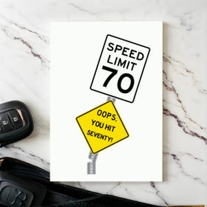 Celebrate their 70th birthday with a humorous 'Oops You Hit 70' Birthday Card, shown next to a pair of car keys. This thoughtful combination adds a memorable touch to their special day, symbolizing the beginning of an exciting journey ahead.