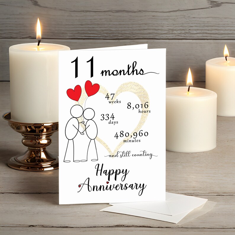 Celebrate your 11 month anniversary with an enchanting card that features a gold heart and intertwined heart balloons held by stick figures. It's presented alongside white candles adding a touch of romance and charm.