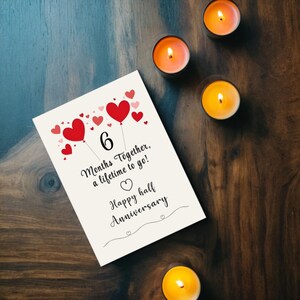 Celebrate your 6-month anniversary with a card featuring vibrant red and pink hearts, a heartfelt message '6 months together, a lifetime to go!' with candles nearby. This elegant design beautifully captures the joy of your milestone.
