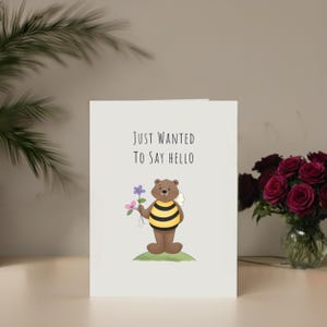 Set in front of colorful flowers, the 'Just Wanted To Say Hello' Card adds a delightful and friendly touch to any gathering.