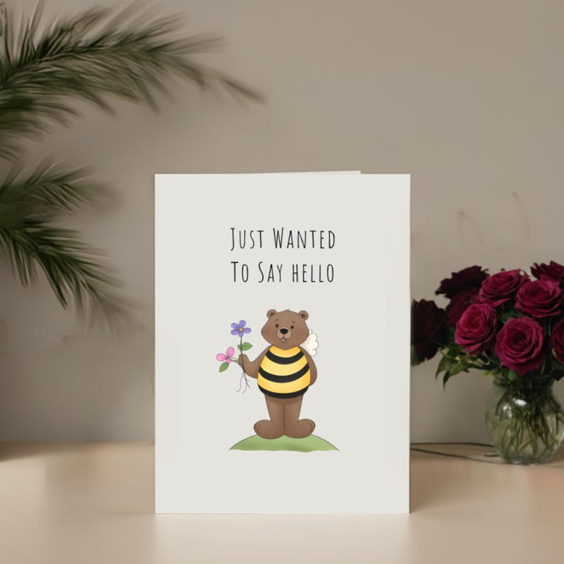 Set in front of colorful flowers, the 'Just Wanted To Say Hello' Card adds a delightful and friendly touch to any gathering.
