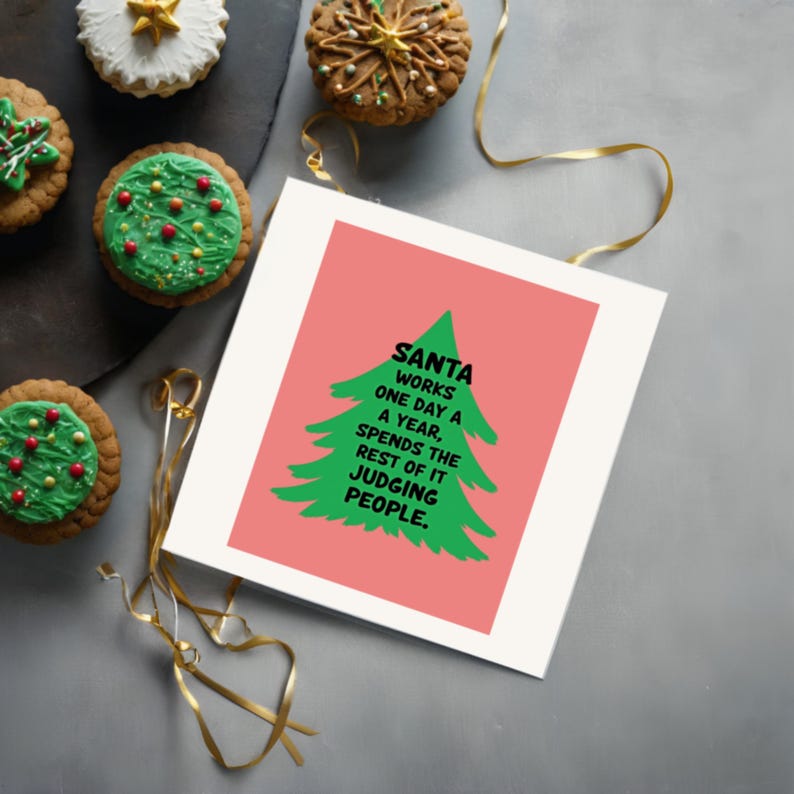 Brighten someone’s holiday with a cheerful Christmas card featuring a playful take on the holiday season! The card has a salmon-colored background that really pops against the large green Christmas tree silhouette in the center. The tree has a rough, hand-painted appearance with jagged edges, giving it a charming and homemade feel. In bold, black, handwritten-style font, the text "SANTA WORKS ONE DAY A YEAR, SPENDS THE REST OF IT JUDGING PEOPLE" . This card is displayed next to festive cupcakes.