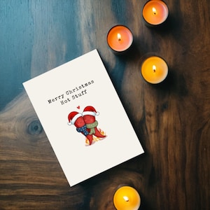 This card features 2 adorable hot peppers hugging in love, with a flame underneath and Santa hats for a holiday touch. The message Merry Christmas Hot Stuff adds a cute vibe, perfect for your partner this Christmas, showcased next to candles.