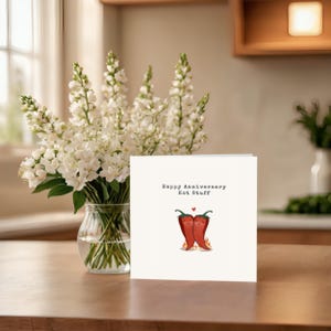 This cute anniversary card, perfect next to white flowers, features 2 adorable hot red peppers hugging with a flame underneath to symbolize fiery love. The message, 'Happy Anniversary Hot Stuff,' adds a romantic touch to your anniversary!