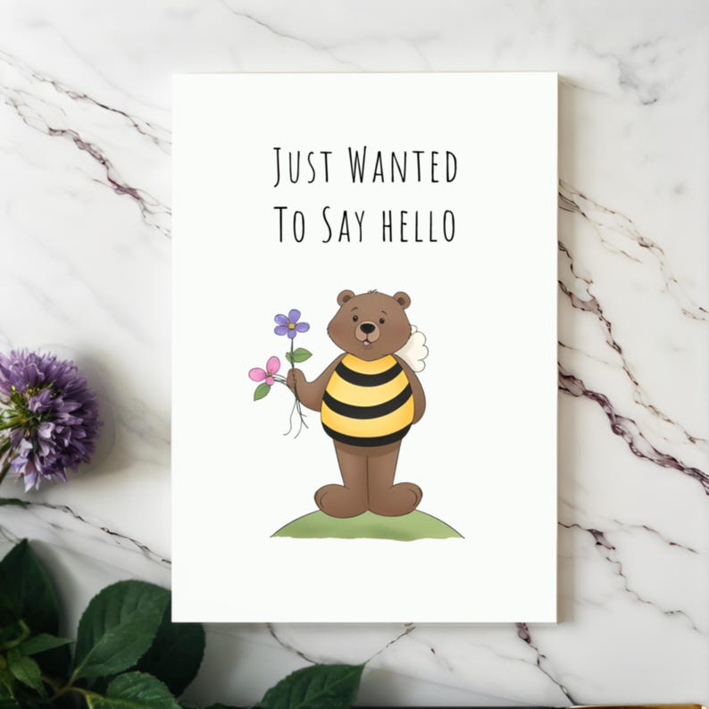 Showcased on a white granite countertop next to vibrant purple flowers, the 'Just Wanted To Say Hello' Card adds a touch of charm and warmth to any occasion