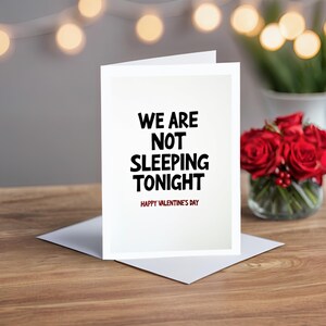 Minimalist Valentine greeting card displayed on a wooden table. The card features bold black text with the phrase We are not sleeping tonight.