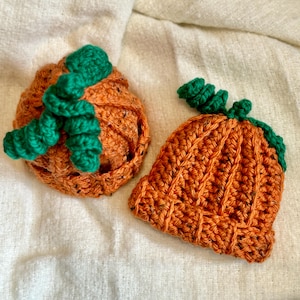 May include: Two crocheted pumpkin hats, one with a green stem and the other with a green stem and leaves. The hats are orange and are made with a chunky yarn.