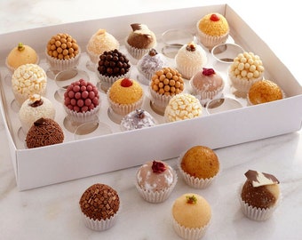 May include: A white box filled with an assortment of colorful, bite-sized treats. The treats are round and covered in various toppings, including sprinkles, coconut flakes, and chocolate. Some are topped with a cherry or a piece of chocolate. The treats are in individual paper cups.