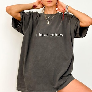 Peut inclure: Un t-shirt surdimensionné gris foncé avec le texte "i have rabies" imprimé en blanc sur le devant.