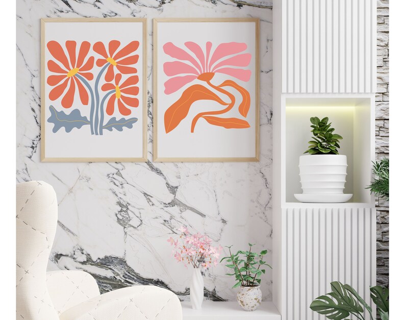 May include: Two framed prints of abstract floral designs. The print on the left features three orange flowers with blue stems and leaves. The print on the right features a single pink flower with orange leaves and stems.