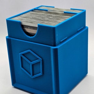 May include: A blue plastic card deck storage box with a cube logo. The box is designed to hold a standard deck of playing cards.