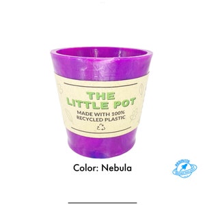 Puede incluir: Una maceta morada hecha de plástico 100% reciclado. La maceta tiene una etiqueta que dice "The Little Pot Made with 100% Recycled Plastic". El color de la maceta es Nebula.