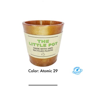 Op de afbeelding: Een bruine plantenpot van gerecycled plastic met een label met de tekst "THE LITTLE POT MADE WITH 100% RECYCLED PLASTIC". De kleur van de pot is Atomic 29.