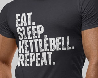 May include: A dark gray t-shirt with a white distressed graphic that reads "Eat. Sleep. Kettlebell. Repeat."