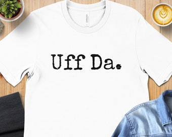 Op de afbeelding: Wit T-shirt met de tekst "Uff Da." in zwart gedrukt.