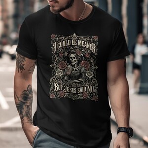 Black t-shirt with skeleton and roses graphic, "I COULD BE MEANER BUT JESUS SAID NO".