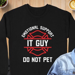May include: A black long-sleeve sweatshirt featuring a red graphic of a Maltese cross emblem. The white text reads "EMOTIONAL SUPPORT IT GUY DO NOT PET" with the words "EMOTIONAL SUPPORT" arched above and "DO NOT PET" positioned below the emblem.