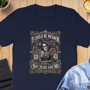 Dark t-shirt with skeleton, roses, and text "I COULD BE MEANER BUT JESUS SAID NO".