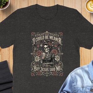 Dark t-shirt with a skeleton and roses design and text "I COULD BE MEANER BUT JESUS SAID NO".