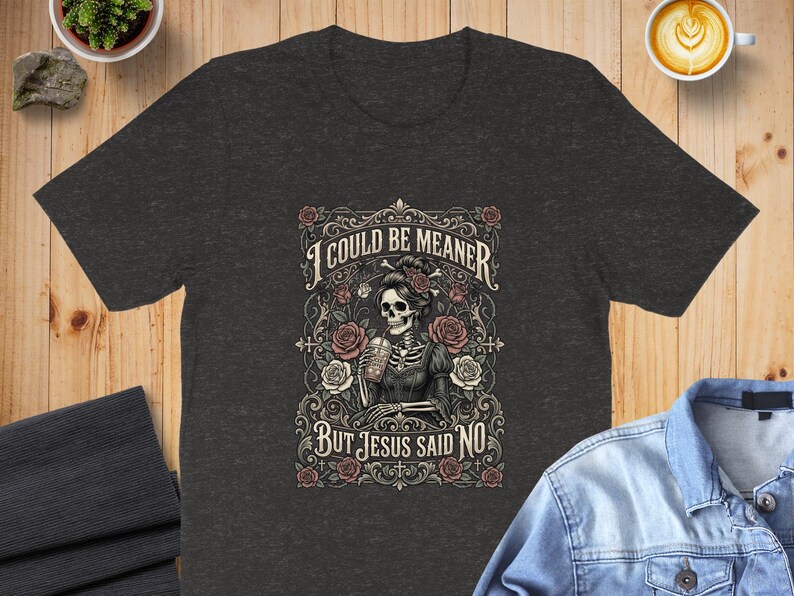 Dark t-shirt with a skeleton and roses design and text "I COULD BE MEANER BUT JESUS SAID NO".