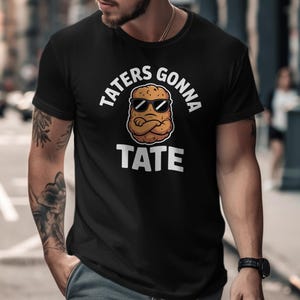 May include: Black t-shirt with the text "TATERS GONNA TATE" in white, above a cartoon potato wearing sunglasses. The potato has crossed arms. The shirt is a crew neck.