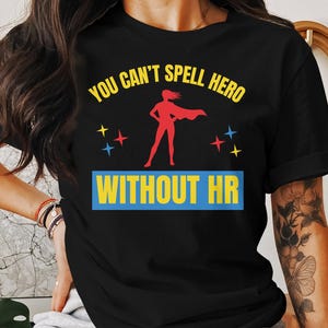 May include: Black t-shirt with a yellow and red graphic of a superhero with the text "You can't spell hero without HR".