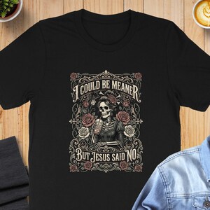 Black t-shirt with a skeleton wearing a crown of roses, text reads "I COULD BE MEANER BUT JESUS SAID NO".