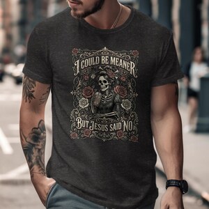 Dark t-shirt with skeleton, roses, and text "I COULD BE MEANER BUT JESUS SAID NO".