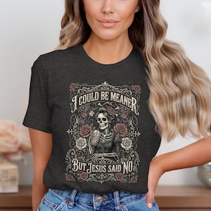Dark t-shirt with skeleton, roses, and text "I COULD BE MEANER BUT JESUS SAID NO".