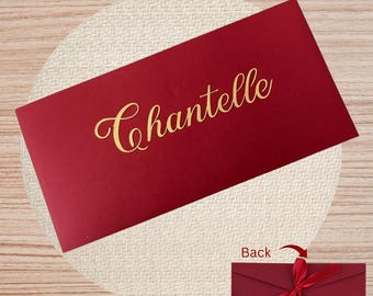 May include: A deep red envelope with the name "Chantelle" in gold script. The envelope rests on a beige woven mat. A smaller image shows the back of the envelope with a red ribbon.