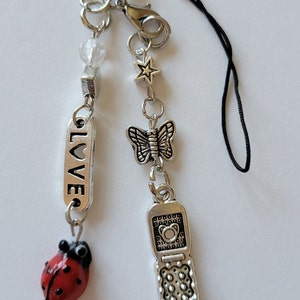 May include: A silver charm bracelet with a black cord, featuring charms of a ladybug, a butterfly, a star, a cell phone, and a charm with the word "LOVE" on it.