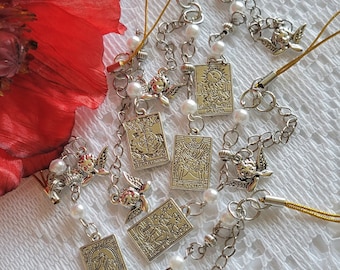 May include: A collection of silver charm bracelets with tarot card charms, angel wing charms, and pearl beads. The charms are attached to gold cords.