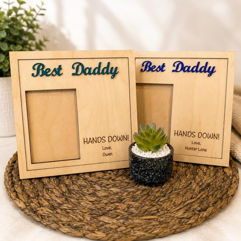 May include: Two wooden picture frames with the words "Best Daddy" in blue script. Each frame has a rectangular opening and the text "HANDS DOWN!" with a name below. A small succulent in a speckled pot sits between the frames.