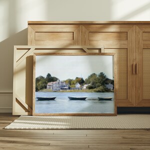 May include: A framed painting of a waterfront scene with a small town in the background. The painting features four boats on the water and a blue sky with white clouds.