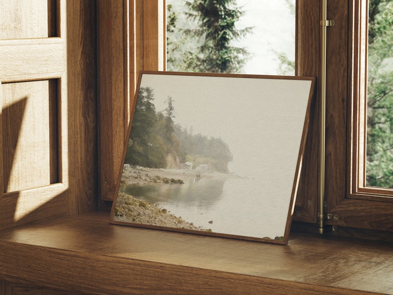 K&ouml;nnte beinhalten: Ein gerahmtes Foto einer nebeligen Strandszene mit felsiger K&uuml;ste und ruhigem Wasser. Das Foto ist in einem Holzrahmen und liegt auf einer Holzfensterbank.