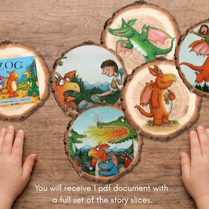 Peut inclure: Tranches de bois illustrées tirées du livre pour enfants "Zog". Les images représentent des dragons colorés et des personnages de l'histoire. Un livre intitulé "Zog" est également inclus. Les tranches sont disposées sur une surface en bois.
